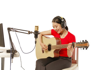 Beautiful Asian woman wearing headphones recording studio playing guitar