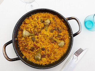  Delicious Spanish paella in traditional paellera, featuring rich mix of rice, saffron, various meats, mushrooms and artichokes, perfect for hearty meal