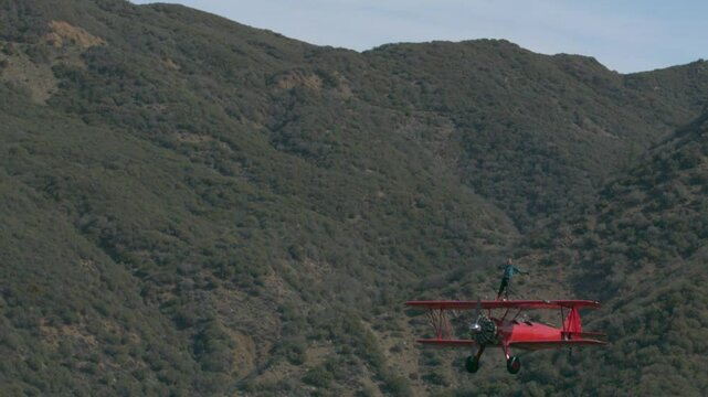 Stunt artist riding on top of a red stearman airplane  over hills - super slow motion