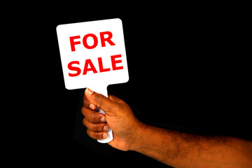 FOR SALE sign board holding hand with black background close-up view, Sale concept photography,...