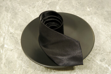 Rolled black necktie over black ceramic plate close up view, Concept photography 
