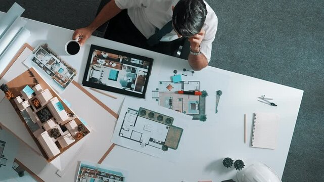 Top view of engineer drink coffee and thinking about house plan at meeting table with equipment and safety helmet scatter around. Aerial view of stressful manager looking at blueprint. Alimentation.