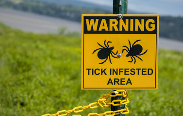 warning tick infested area sign in grassy area near the hudson river westchester county upstate new york (lyme disease carrying parasite insect bug) © Yuriy T