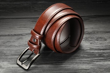 One brown leather belt on wooden table, closeup