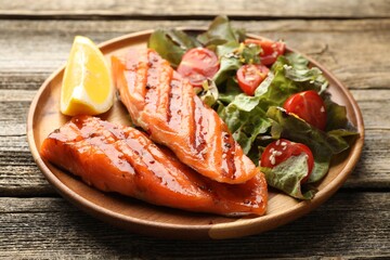Seafood. Tasty grilled salmon served with salad and lemon on wooden table, closeup