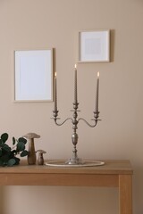 Stylish candlestick with burning candles and other decor on wooden table near beige wall indoors