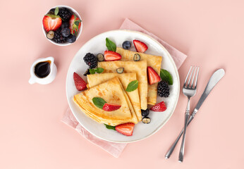 French breakfast crepes with strawberries, blackberries and maple syrup on pink background. Top view