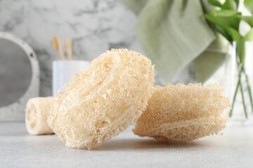 Different loofah sponges on light grey table, closeup