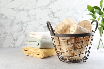 Different loofah sponges in basket and towels on light grey table