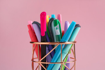 Different stationery in pen holder on pink background, closeup