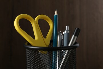 Pens and other stationery in holder on blurred background, closeup