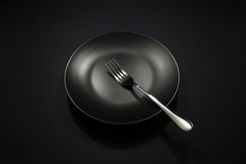 Fork on plate isolated on dark background close-up shot, Empty black plate with silver fork,...