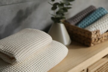 Waffle towels and vase with branches on wooden dresser near grey wall, closeup
