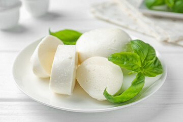 Pieces of delicious mozzarella cheese and basil on white wooden table, closeup