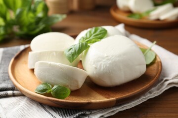 Pieces of delicious mozzarella cheese and basil leaves on wooden table, closeup