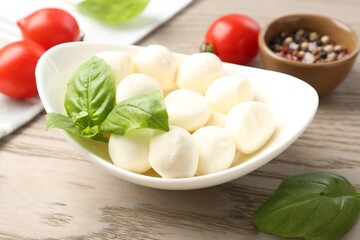 Tasty mozzarella cheese balls, tomatoes, basil and peppercorns on wooden table, closeup