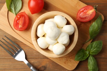 Tasty mozzarella balls, tomatoes and basil on wooden table, flat lay