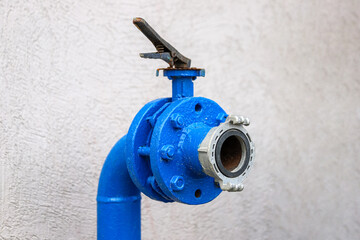 Closeup of the blue water pipe valve for water flow control against a white wall.