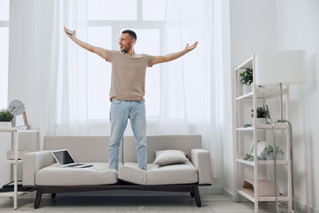 A joyful man stands on a couch, embracing life amidst a digital detox. His expression reflects...