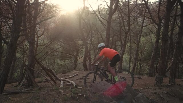 Slow Motion of Male Mountain Biker Riding Through Forest at Sunse