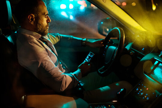 Sleepy distracted and tired middle aged caucasian businessman driving a car at night and using his phone