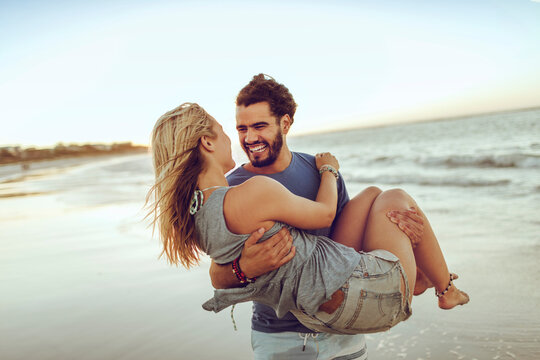 Young couple on a date having fun on a sandy beach next to the ocean during sunset