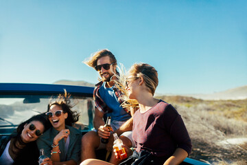 Young and diverse group of people on a spring break road trip in the back of a truck drinking beers and having fun
