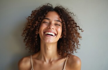 Joyful young woman with curly hair laughs heartily. Happy, candid portrait of beautiful female smiles. Expressive portrait of youthful woman, smiling. Genuine emotion, positive vibes studio.