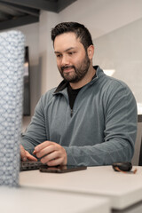 Naklejka premium A tech-savvy young man concentrates on his laptop, developing software in a lively coworking hub filled with startup energy.