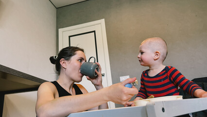 A loving mother feeds her little son with a spoon as they sit together in a cozy kitchen.