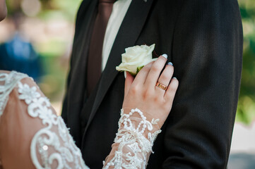 Romantic Wedding Scene: Couple's Hands with Rings, White Rose Boutonniere, Formal Attire, Lace Dress, Outdoor Garden Setting