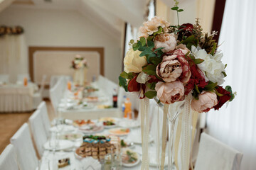 Elegant Wedding Table Setting with Tall Floral Centerpiece, Ivory and Burgundy Blooms, Banquet Hall, Champagne Glasses, Celebration.