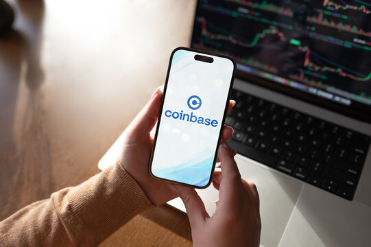 Woman holding smartphone with coinbase app and stock chart on laptop screen