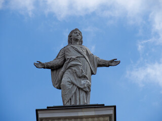 Historic religious statue with outstretched arms stands majestically against blue sky with white...
