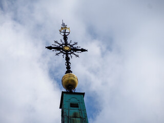Orthodox church golden dome topped with ornate black metal cross against dramatic cloudy sky