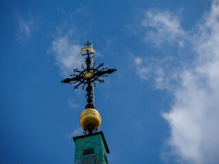 Green patina church dome with golden sphere and elaborate orthodox cross under blue sky