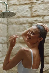 Gordijnen smiling woman enjoying outdoor shower with wet hair, natural stone background, warm lighting, relaxed mood, casual white swimsuit, summer freshness © SHOTPRIME STUDIO