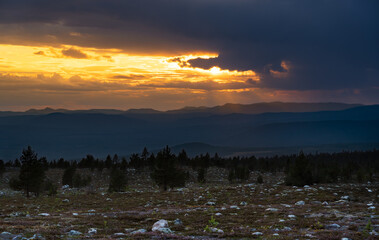 A stunning sunset casts golden hues across the Norwegian mountains viewed from Sweden, showcasing the rugged beauty of Scandinavian wilderness during the peaceful summer evening.
