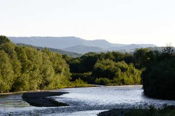 Serene bend of a river surrounded by rich greenery and layered mountain ridges, ideal for eco,...