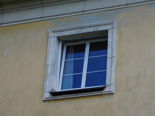 White framed window with blue glass reflection on cream colored European building facade