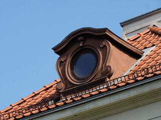 Traditional European red tile roof with decorative round dormer window against clear blue sky