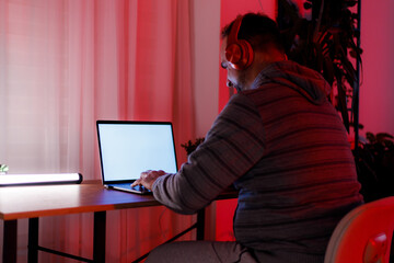 Man working on laptop in dimly lit room with red lighting