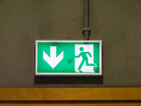 Green emergency exit sign with running figure and arrow illuminated on concrete wall in modern building
