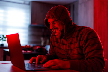 Man in hoodie laughing while using laptop in dimly lit room