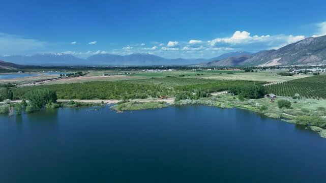 Aerial lake farm fruit orchard Utah mountain valley fast 4K. Orchard, farms and rural ranch property. Lake used for irrigation and recreation. Rural landscape in mountain valley. Agricultural. 