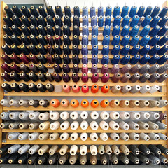 Colorful thread spools arranged on a shelf, a vibrant spectrum ideal for sewing, textile design, or crafting projects. Shows organization and color variations.
