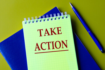 TAKE ACTION - words in yellow notebook on blue notebook and pen background