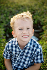 A summer portrait of a cheerful blond boy in a checkered shirt.