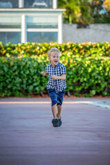 A summer portrait of a cheerful blond boy in a checkered shirt.