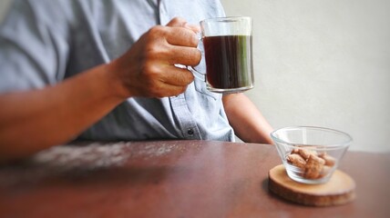 Man at table holding up a cup of black coffee accompanied by a plate of snacks. Morning coffee illustration.